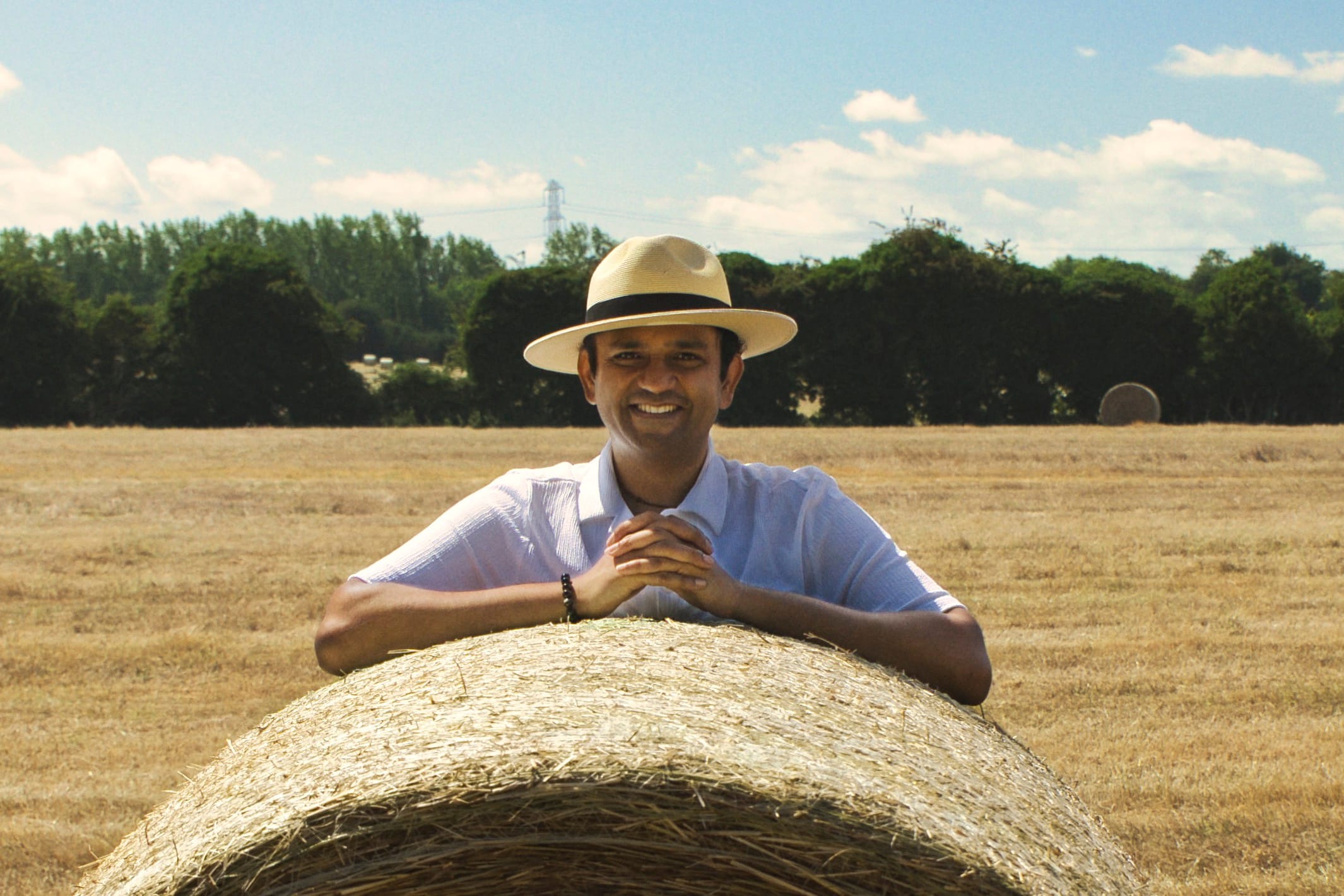 Aditya Rajashekaran leaning on a hay bale in a harvested field