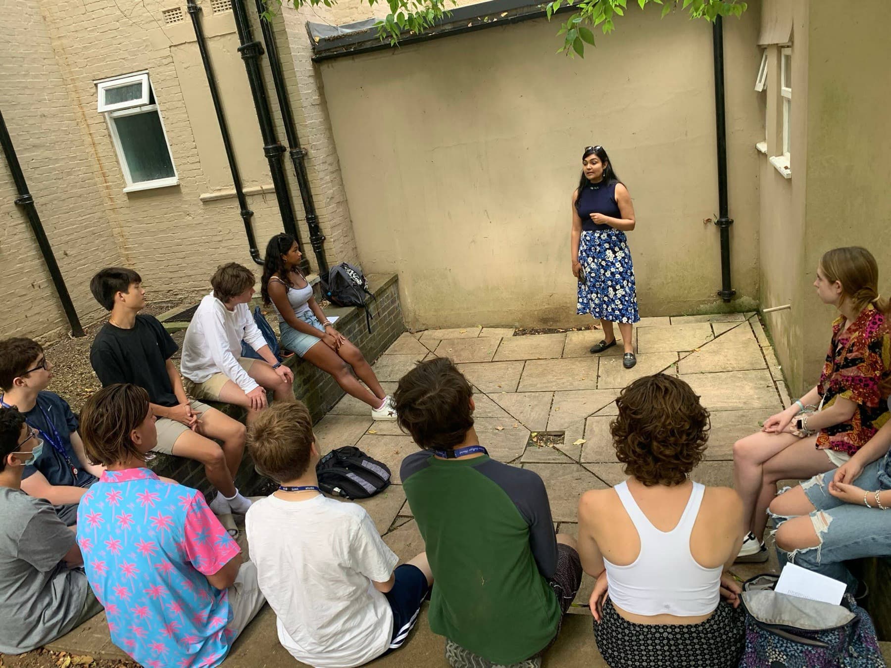 Dr Ayushi Agarwal leading a taster session in an Oxford courtyard, a circle of teenagers seated around her